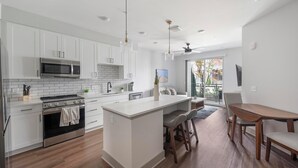 Una cocina moderna con armarios blancos, una isla central y una zona de comedor con mobiliario de madera.