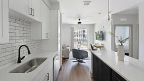 A modern kitchen with white cabinets, a black faucet, and a dining area with a table and chairs. - Landing | Chic 1BD, Gym, Courtyard (Nashville)
