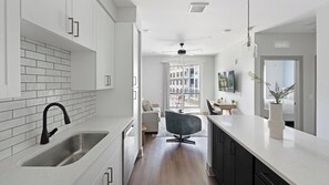 A modern kitchen with white cabinets, a black faucet, and a dining area with a table and chairs. - Landing | Stylish 1BD, Courtyard, Gym (Nashville)