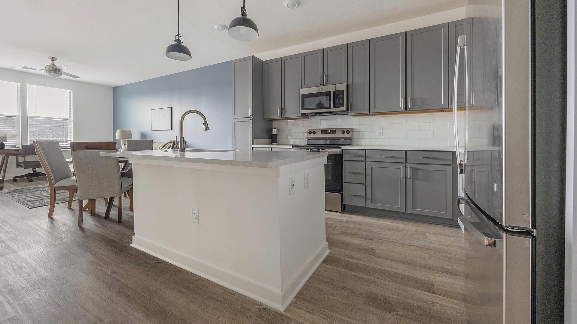Uma cozinha moderna com armários cinza, uma ilha central, eletrodomésticos de aço inoxidável e iluminação pendente.