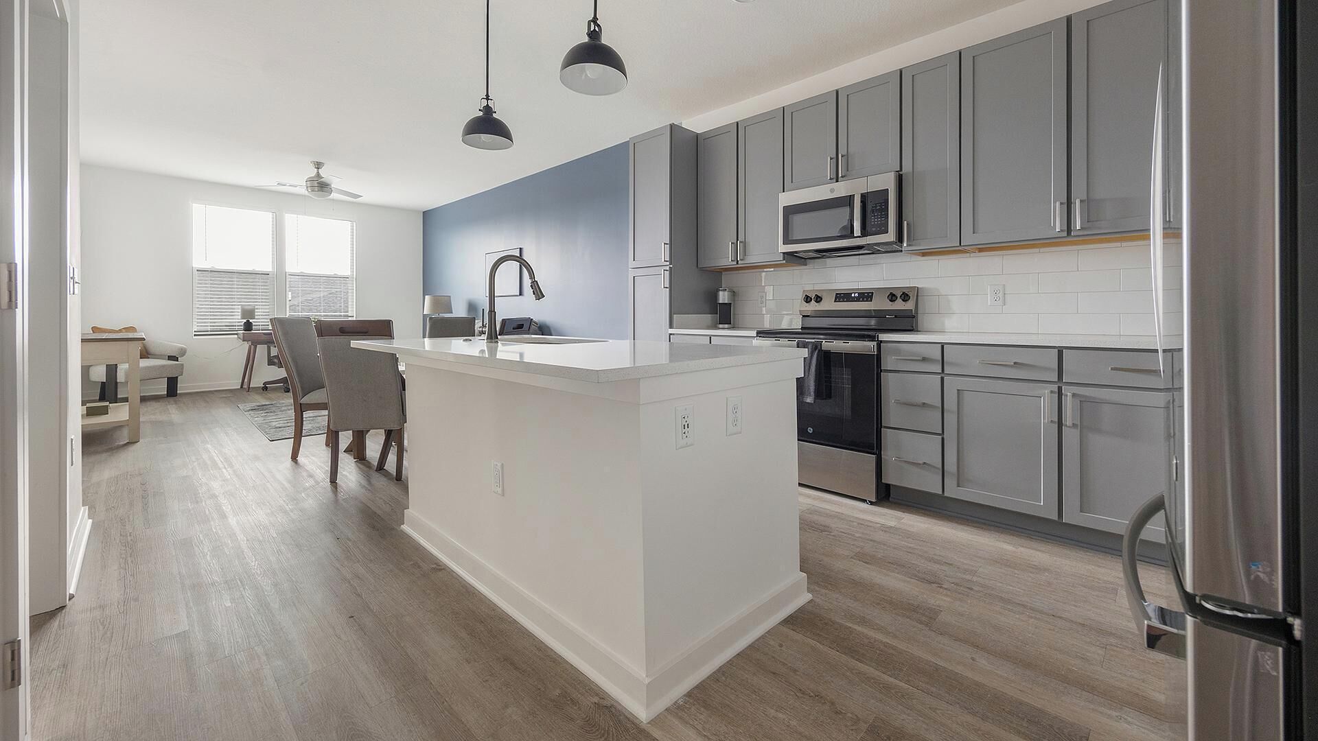 Een moderne keuken met grijze kastjes, een centraal eiland, roestvrijstalen apparatuur en een eethoek met een tafel en stoelen.