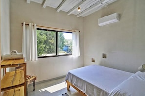 Ein Schlafzimmer mit Bett, einem Vorhangfenster, einem Holztisch und einer Klimaanlage.