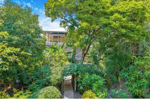 A lush garden with a wooden bridge leading to a building with a sloped roof. - 2BR Santa Teresa Apartment Walk to Beach. AC & WiFi (Santa Teresa)