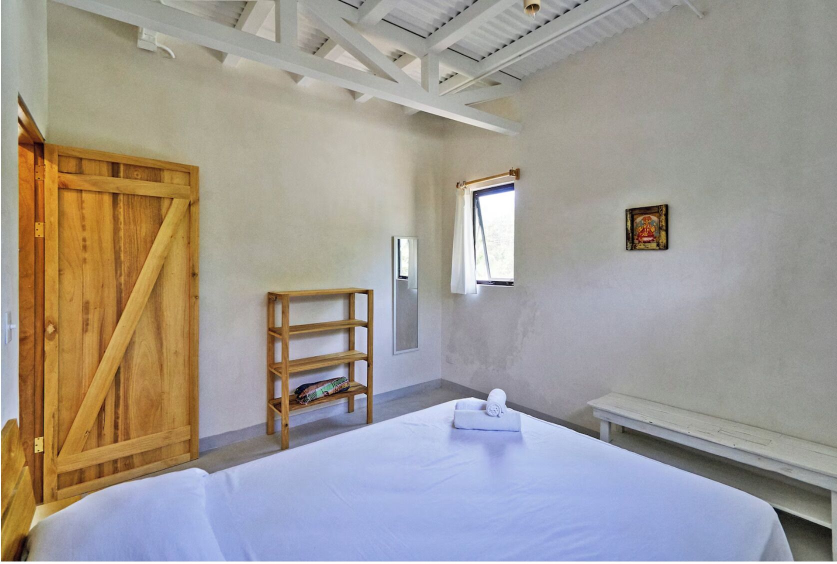 A bedroom with a bed, a wooden wardrobe, a shelf, a window, and a picture on the wall.