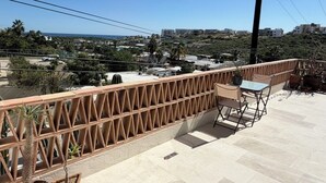 Een dakterras met uitzicht op een kustplaatsje, een houten hekwerk en een tafel met stoelen.