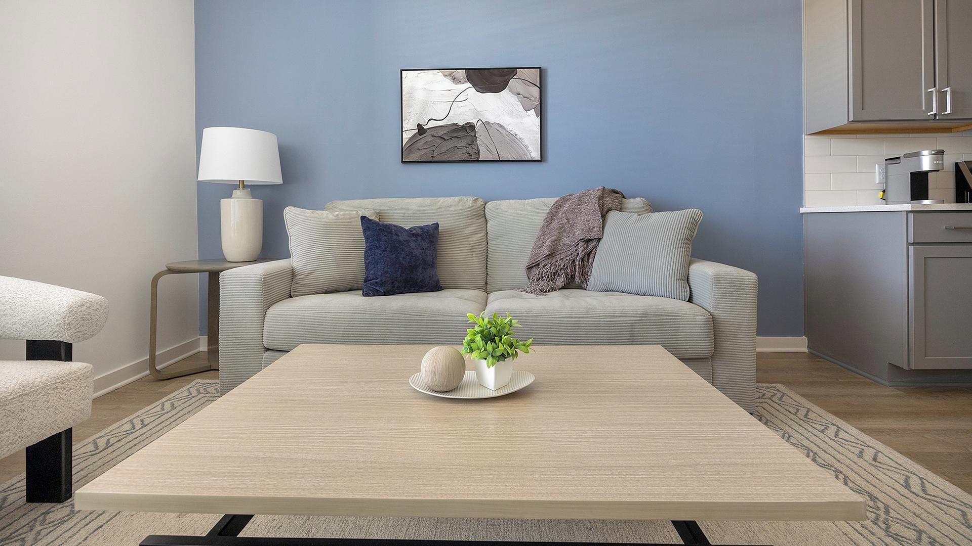 Un salon avec un canapé, une table basse, une lampe et, au fond, un coin cuisine.