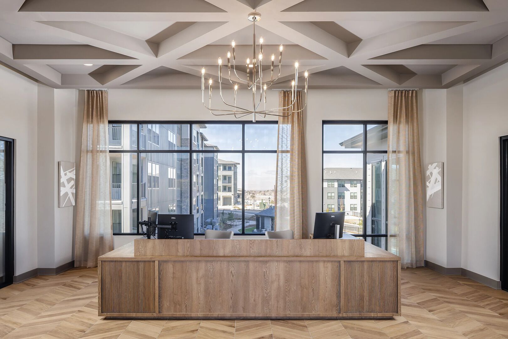 Un hall d’hôtel moderne avec un comptoir d’accueil en bois, de grandes fenêtres et un lustre.
