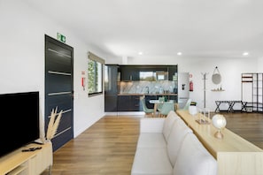 Ein modernes Wohnzimmer mit Flachbildfernseher, einer Couch, einem Couchtisch aus Holz und einer Küche im Hintergrund.