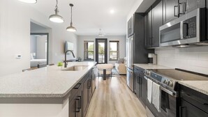 A modern kitchen with a large island, dark cabinetry, stainless steel appliances, and a view to the outdoors. - Landing | Beautiful 1BD, Game Room, Clubhouse (Leander)