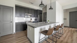 Una cucina moderna con mobili scuri, elettrodomestici in acciaio inossidabile, un'isola in granito con sgabelli da bar e una lampada a sospensione.