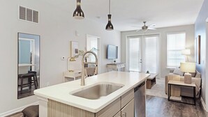 Cocina moderna con una isla grande, electrodomésticos integrados, iluminación colgante y un comedor con sofá y mesa.