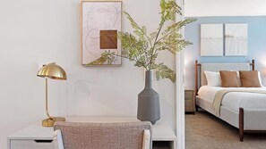 A bedroom with a bed, bedside table, lamp, and a vase with greenery.