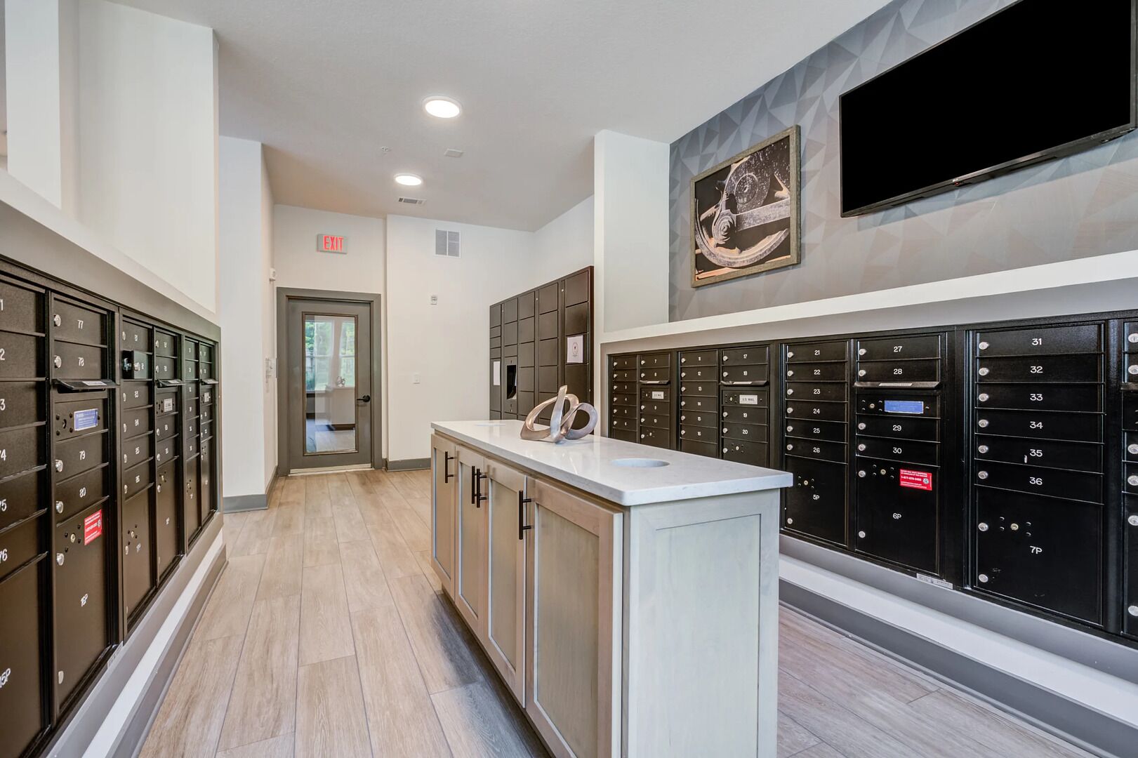 A hallway with a row of dark-colored lockers on both sides, a white reception desk, and a framed artwork on the wall.