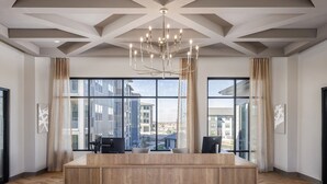 A modern hotel lobby with a wooden reception desk, large windows, and a chandelier. - Landing | Spectacular 1BD, Clubhouse, Yoga Studio (Broomfield)