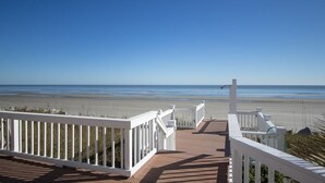 Een houten terras met witte leuningen met uitzicht op een strand.