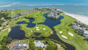 Luchtbeeld van een kustresort met een golfbaan, diverse waterpartijen, een strand en woonwijken.