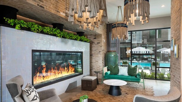 A modern lounge area with a large fireplace, comfortable seating, and a view of a swimming pool. - Landing | Beautiful 1BD, Game Room (Houston)