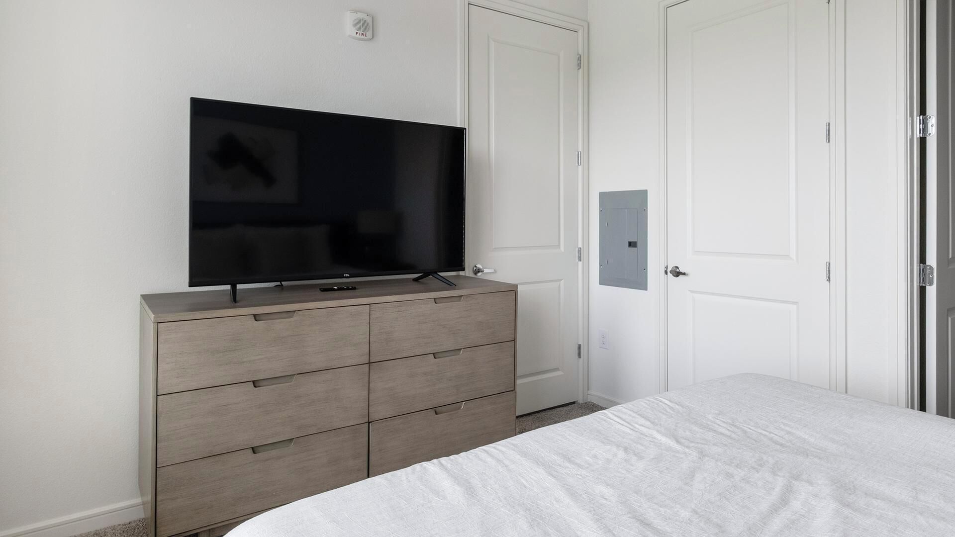 Une chambre à coucher avec un lit, une commode, un téléviseur et une porte.