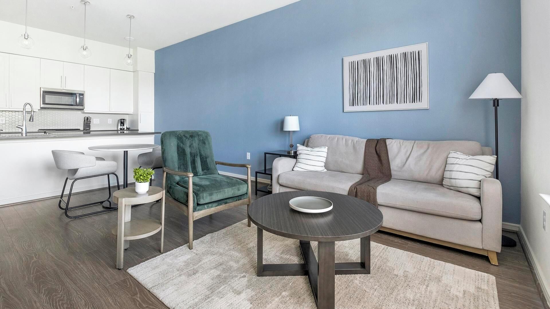 A modern living room with a sofa, a green chair, a dining table, and a kitchen area in the background.