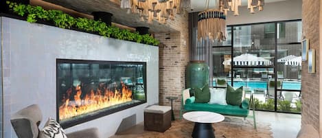 A modern lounge area with a large fireplace, comfortable seating, and a view of a swimming pool.