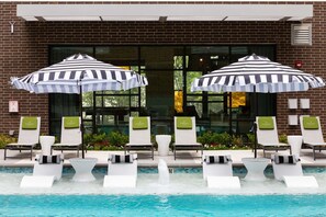 Ein Poolbereich mit Liegestühlen und gestreiften Sonnenschirmen, eine Ziegelhausfassade und freie Sicht auf den Pool.