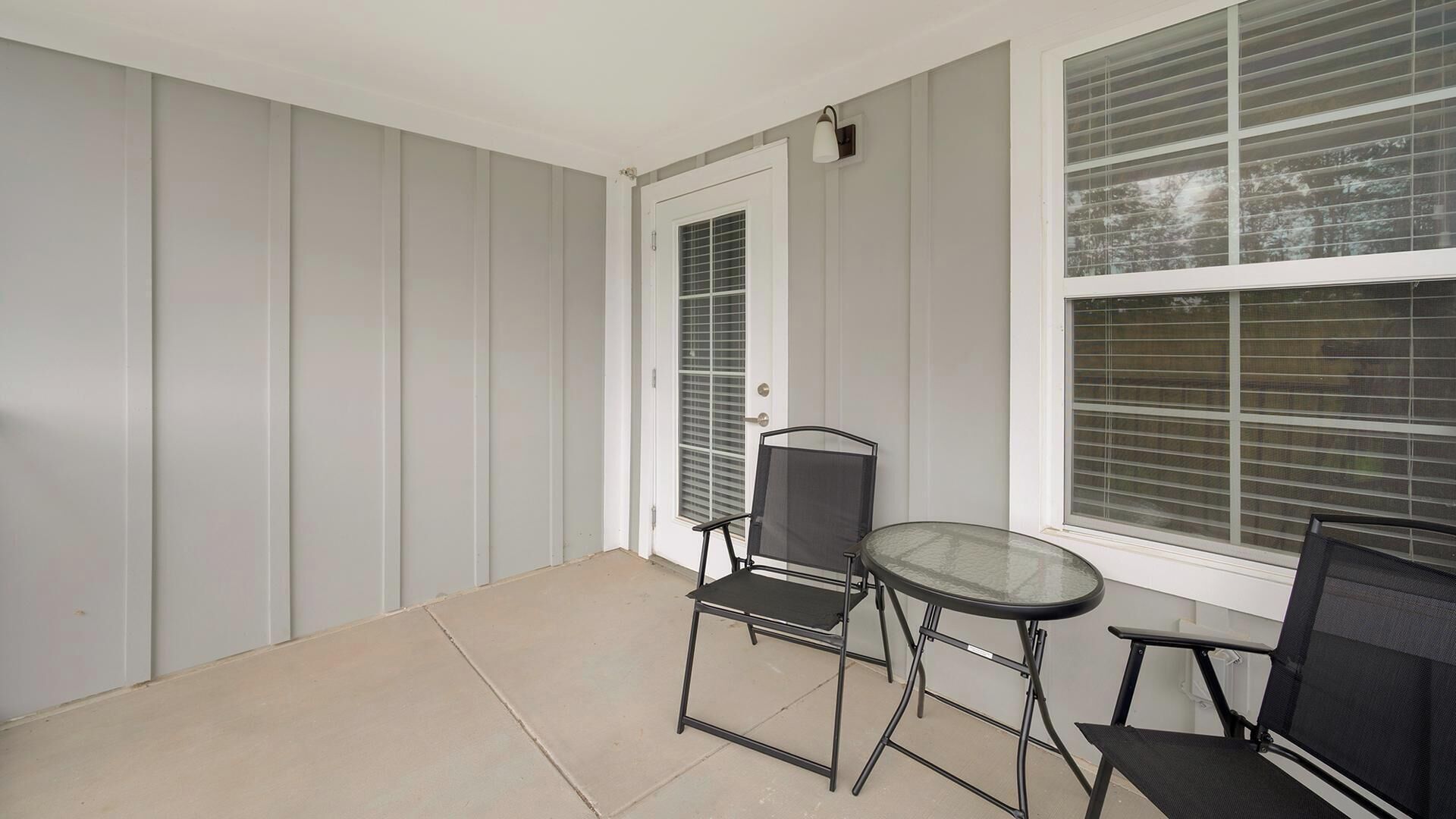A covered patio with a door, a chair, a table, and a window with blinds.