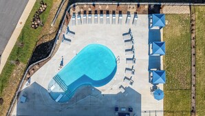 Vue aérienne d’un espace piscine avec des chaises longues et des parasols, entouré d’un jardin clos.