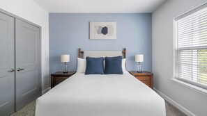 A bedroom with a bed, two bedside tables, a nightstand, a door, and a window with blinds. - Landing | Stylish 2BD, Clubhouse, Pool (Ooltewah)