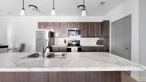 A modern kitchen with a marble island, stainless steel appliances, and wooden cabinets. - Landing | Stunning 2BD, Pool, Clubhouse (Ooltewah)
