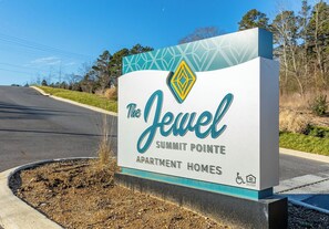 A sign for The Jewel Summit Pointe Apartment Homes with a geometric design and a wheelchair accessibility symbol. - Landing | Beautiful 2BD, Pool, Clubhouse (Ooltewah)