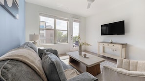 A modern living room with a sofa, coffee table, TV, and a view through the window. - Landing | Modern 1BD, Clubhouse (Austin)