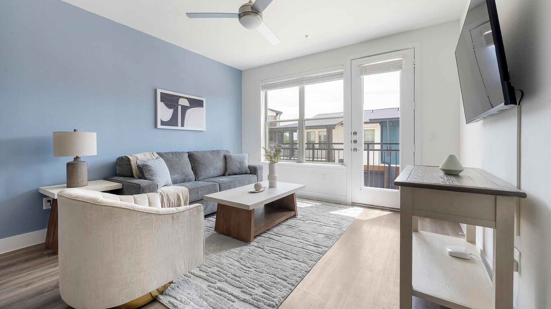 En moderne stue med sofa, lænestol, sofabord og et fjernsyn ophængt på væggen.