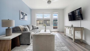 A modern living room with a grey sofa, a coffee table, a TV, and a balcony with a view. - Landing | Amazing 1BD, Clubhouse (Austin)
