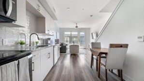 A modern kitchen with a black stove, white cabinets, and a dining area with a wooden table and chairs. - Landing | Amazing 1BD, Clubhouse (Austin)