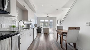 A modern kitchen with a black stove, white cabinets, and a dining area with a wooden table and chairs. - Landing | Stunning 1BD, Clubhouse (Austin)