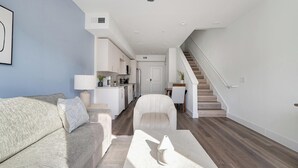 Ein modernes Wohnzimmer mit einer Couch, einem Sessel und einer Treppe, die in einen Küchenbereich führt.
