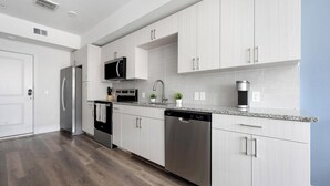 A modern kitchen with stainless steel appliances, white cabinetry, and a granite countertop. - Landing | Chic 1BD, Clubhouse (Austin)