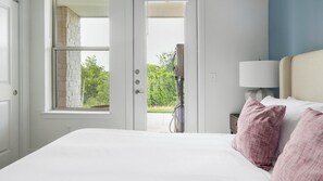A bedroom with a bed, a nightstand, a lamp, and a view of the outdoors through a door. - Landing | Modern 1BD, Clubhouse (Austin)