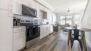 A modern kitchen with stainless steel appliances, a dining area with a table and chairs, and a view of the outside through large windows. - Landing | Chic 1BD, Clubhouse (Austin)