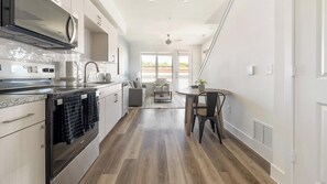 A modern kitchen with a built-in oven, a dining area with a table and chairs, and a view of the outdoors through large windows. - Landing | Chic 1BD, Clubhouse (Austin)