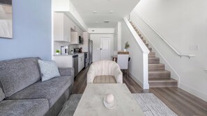 Un salon moderne avec un canapé gris, une table basse blanche et un escalier menant à un deuxième étage.