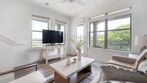 Ein modernes Wohnzimmer mit Flachbildfernseher, Couchtisch, Sofa und großen Fenstern.