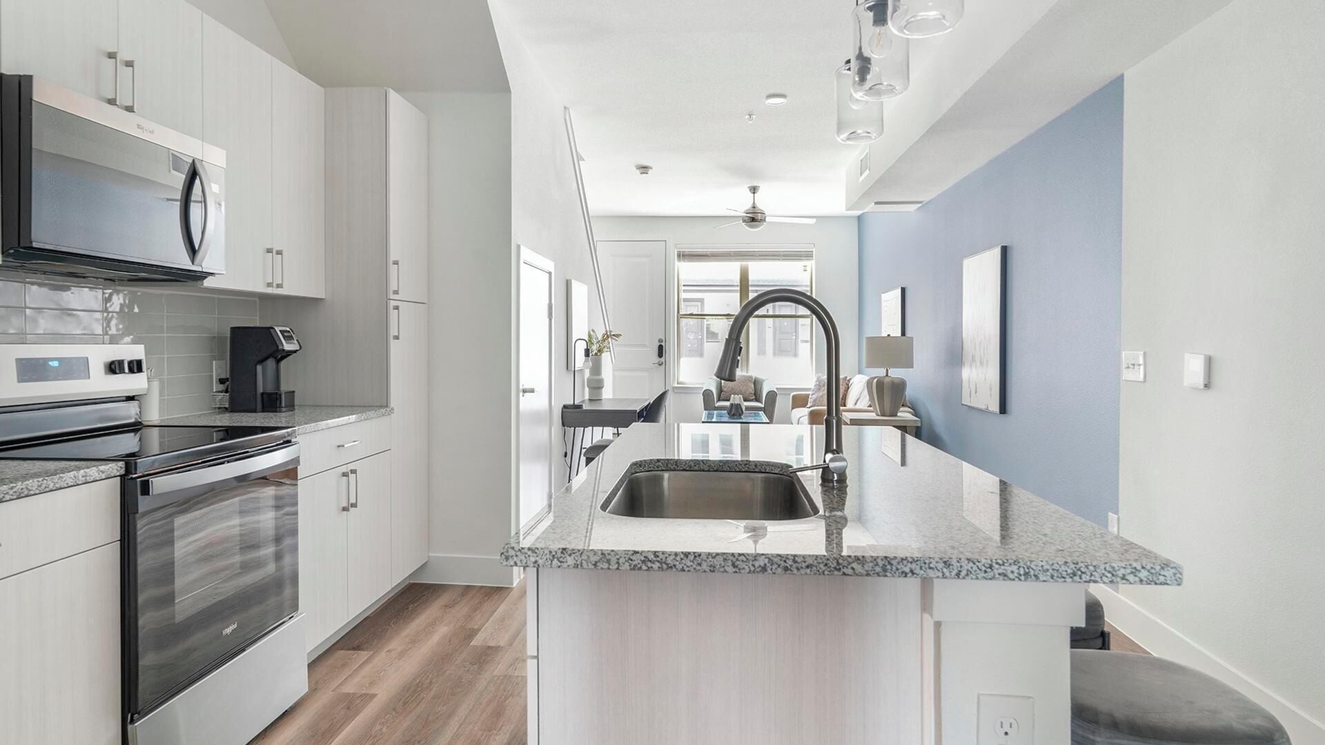 A modern kitchen with stainless steel appliances, a granite countertop, and a view into the living area.