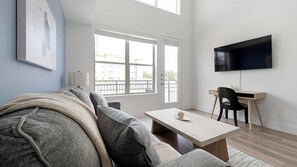 A modern living room with a sofa, a coffee table, a TV, and a desk. - Landing | Stylish 1BD, Clubhouse (Austin)