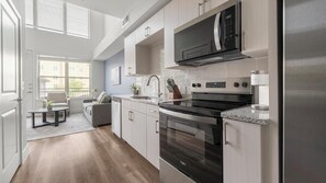 A modern kitchen with stainless steel appliances, a dining area with a sofa and table, and a view of the outside through large windows. - Landing | Chic 1BD, Clubhouse (Austin)