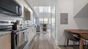Eine moderne Küche mit Backofen, ein Essbereich mit Holztisch und Blick auf die Stadt durch große Fenster.