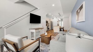 Ein modernes Wohnzimmer mit einer Couch, einem Couchtisch, einem an der Wand montierten Fernseher und einer Treppe.