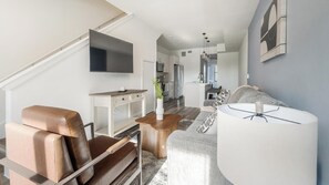 Ein modernes Wohnzimmer mit einer Couch, einem Couchtisch, einem Fernseher und einer Küche im Hintergrund.