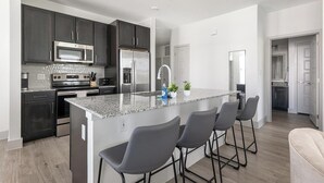 Una cocina moderna con armarios oscuros, electrodomésticos de acero inoxidable y una isla de granito con taburetes de bar.