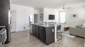 Eine moderne Küche mit einer zentralen Kochinsel, einem Essbereich mit Tisch und Stühlen sowie einem Wohnbereich mit einer Couch.